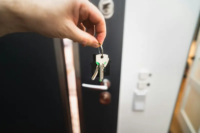 Personne tenant un trousseau de clés devant une porte d'entrée entrouverte