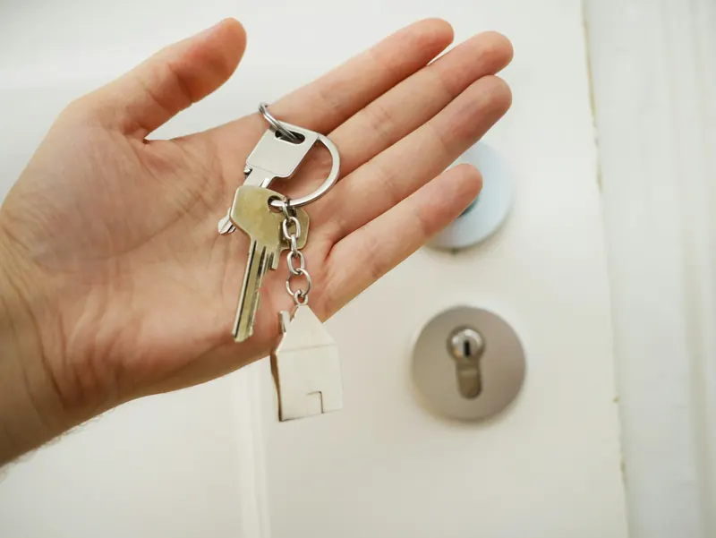 Main tenant un trousseau de clés devant le cylindre d'une porte d'entrée